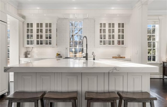 bar with backsplash, sink, light stone counters, dark hardwood / wood-style floors, and crown molding