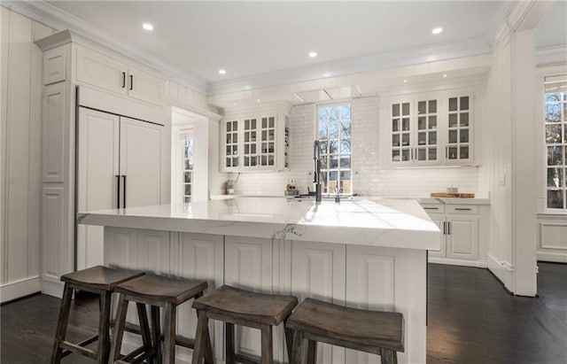 kitchen with a kitchen bar, backsplash, dark hardwood / wood-style floors, kitchen peninsula, and white cabinets