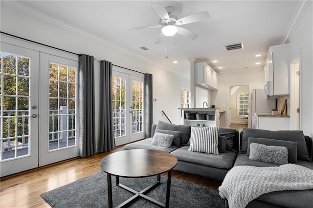 living room with light wood-type flooring, ornamental molding, french doors, and a healthy amount of sunlight