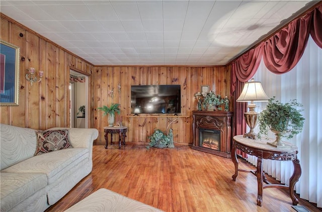 living room with light wood-style flooring, wooden walls, and a warm lit fireplace