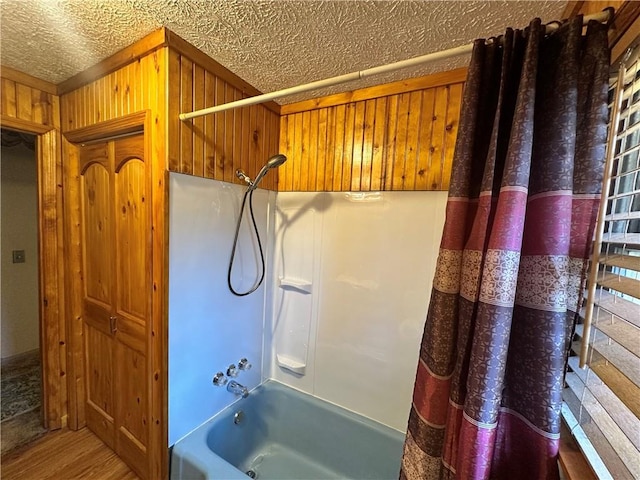 bathroom with wood finished floors, shower / bath combo with shower curtain, a textured ceiling, and wood walls