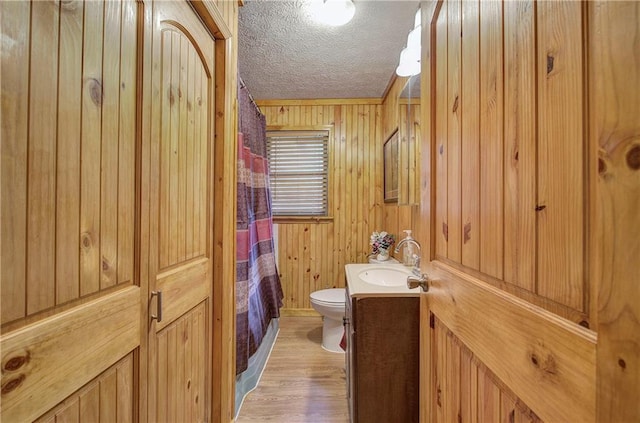 bathroom with wood walls, a textured ceiling, hardwood / wood-style floors, vanity, and toilet