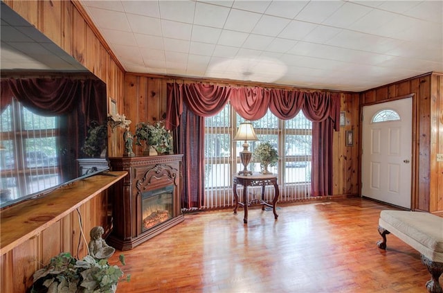 foyer with a glass covered fireplace, crown molding, light wood-style floors, and wood walls