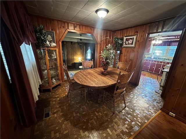 dining space featuring visible vents, arched walkways, parquet floors, and wood walls