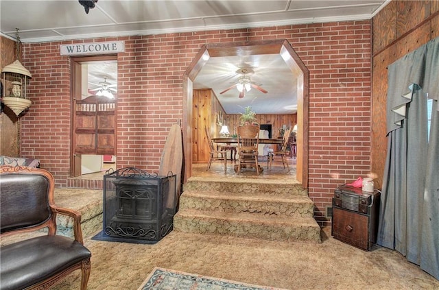 living room with carpet, ornamental molding, a wood stove, wood walls, and brick wall