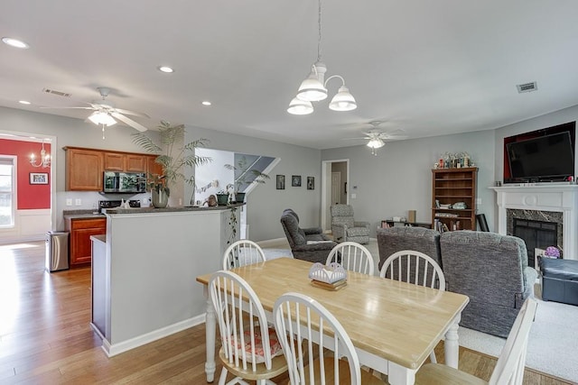 dining room with a ceiling fan, a chandelier, light wood-style flooring, a premium fireplace, and recessed lighting
