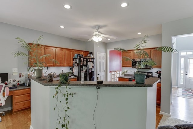 kitchen featuring black appliances, light wood-style floors, a desk, dark countertops, and recessed lighting