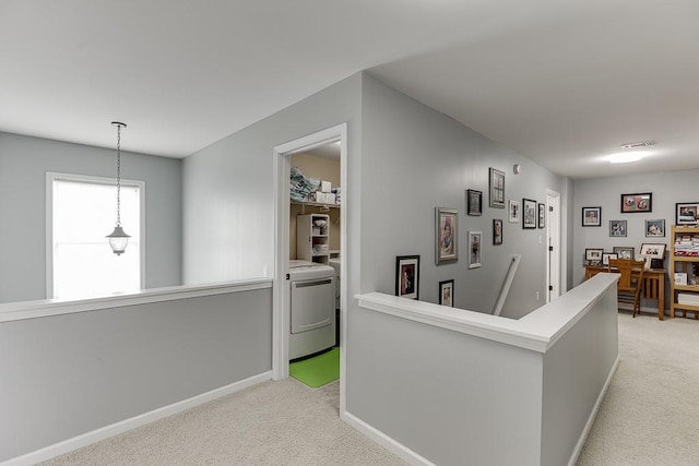 hallway featuring washer / dryer, an upstairs landing, light carpet, and baseboards