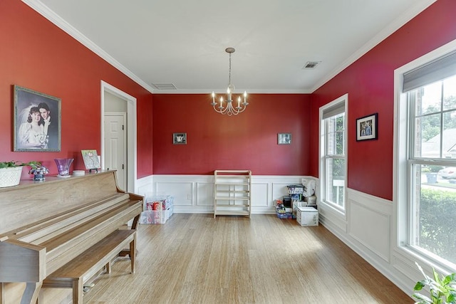 dining space with a chandelier, ornamental molding, wainscoting, wood finished floors, and a decorative wall