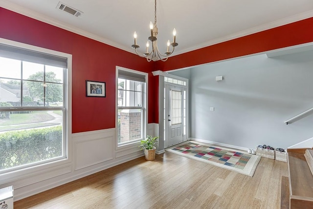 entryway with a chandelier, wood finished floors, wainscoting, plenty of natural light, and crown molding