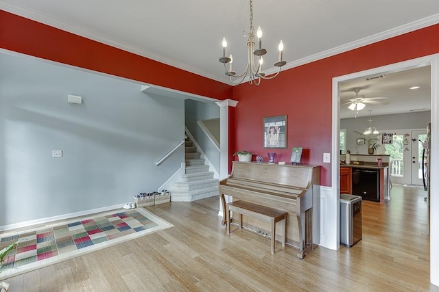 dining room with light wood-type flooring, stairway, a chandelier, ornamental molding, and a ceiling fan