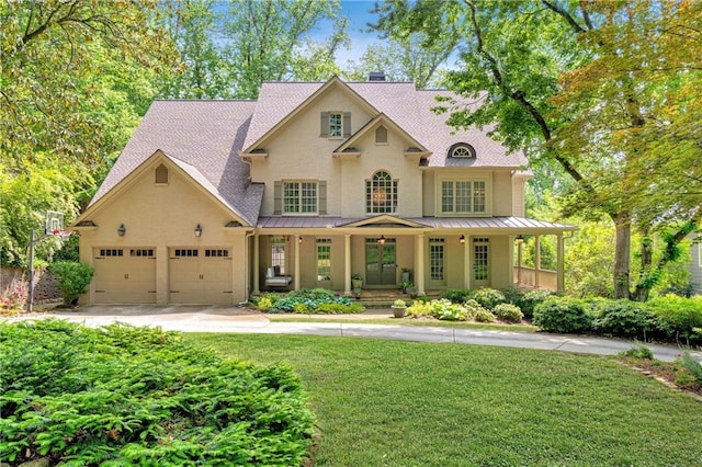 view of front of property with covered porch, a standing seam roof, driveway, a front yard, and an attached garage