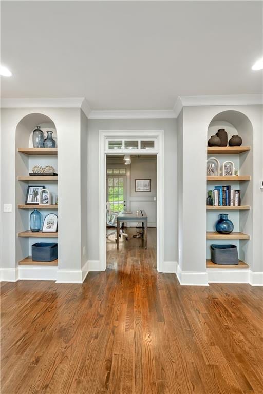 corridor featuring crown molding, built in features, dark wood finished floors, and baseboards
