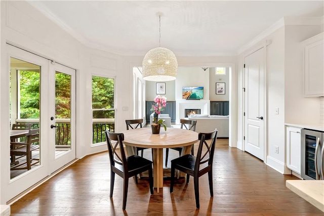 dining space featuring beverage cooler, a warm lit fireplace, ornamental molding, and dark wood-style flooring