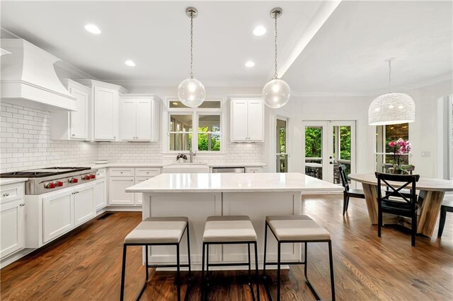 kitchen with custom exhaust hood, a breakfast bar, appliances with stainless steel finishes, light countertops, and backsplash