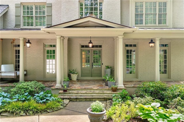 view of exterior entry with a porch, french doors, and brick siding