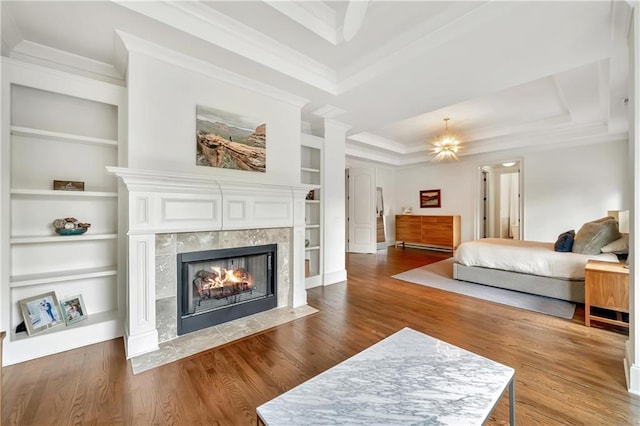 bedroom with a raised ceiling, a tile fireplace, wood finished floors, and crown molding