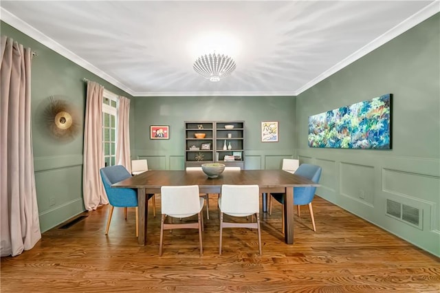 dining room featuring wood finished floors, visible vents, a decorative wall, and crown molding