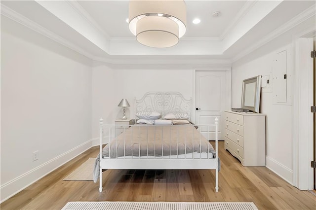 bedroom featuring baseboards, ornamental molding, light wood finished floors, and a tray ceiling