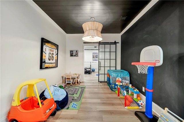 rec room with ornamental molding, visible vents, wood finished floors, and a barn door