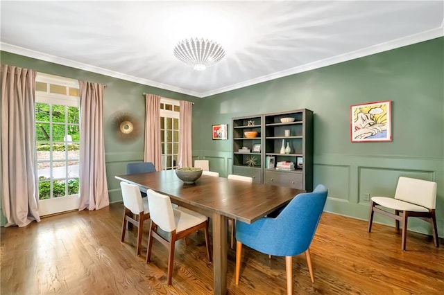 dining room with ornamental molding, a wainscoted wall, wood finished floors, and a decorative wall