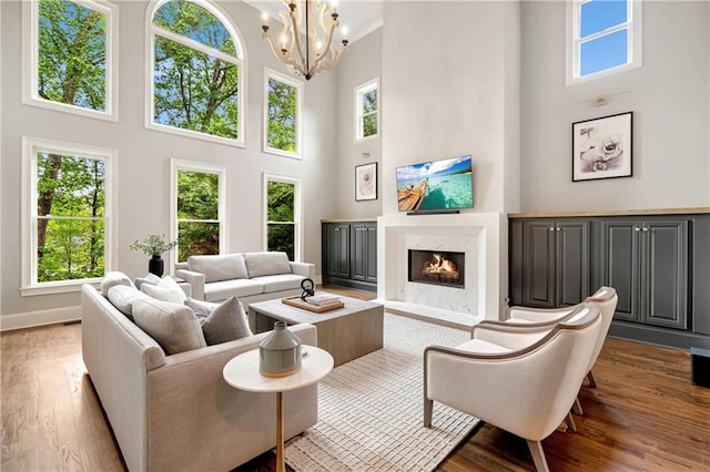 living area with wood finished floors, a chandelier, a fireplace, baseboards, and a high ceiling
