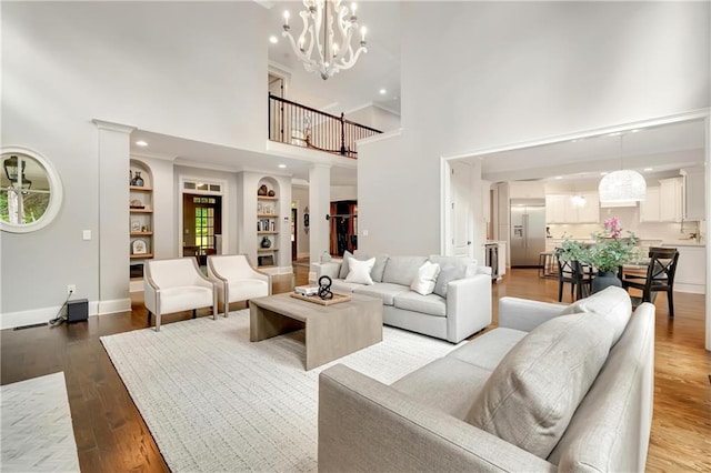 living room with light wood-style floors, built in shelves, a notable chandelier, baseboards, and a towering ceiling
