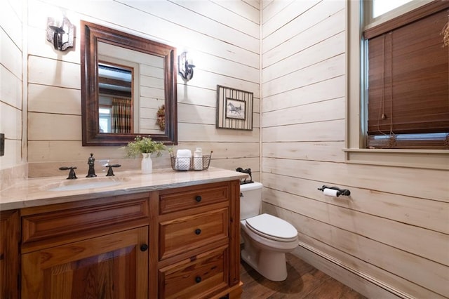 bathroom with large vanity, wood walls, toilet, and hardwood / wood-style flooring