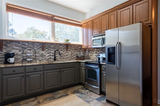 kitchen with stainless steel appliances, stone countertops, dark tile flooring, gray cabinetry, and backsplash