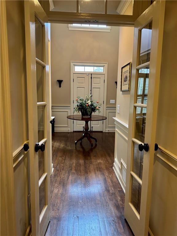 foyer with a wainscoted wall, a decorative wall, dark wood-type flooring, and french doors