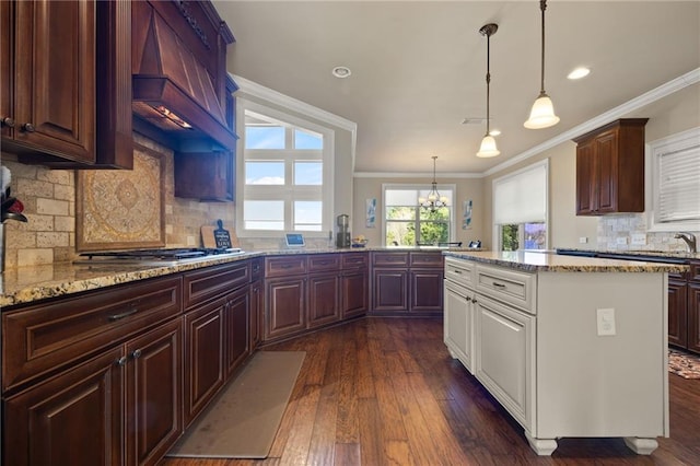 kitchen featuring stainless steel gas cooktop, hanging light fixtures, ornamental molding, dark hardwood / wood-style floors, and light stone countertops