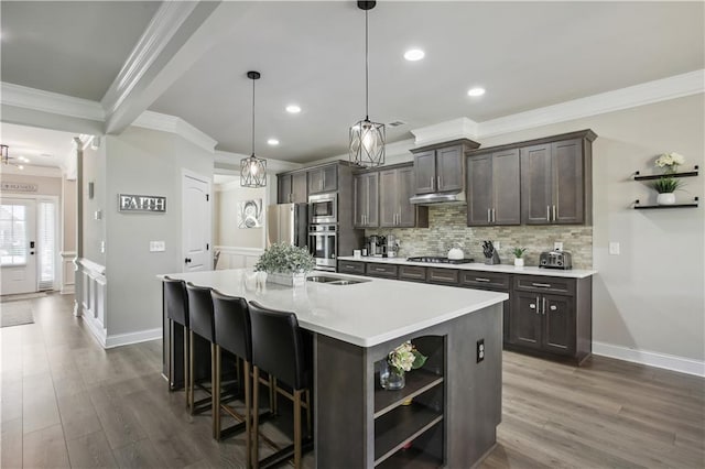 kitchen featuring tasteful backsplash, an island with sink, ornamental molding, stainless steel appliances, and open shelves