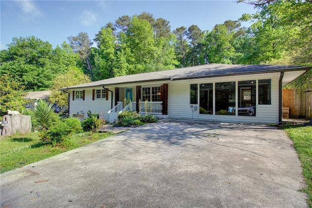 ranch-style house featuring covered porch, concrete driveway, and fence