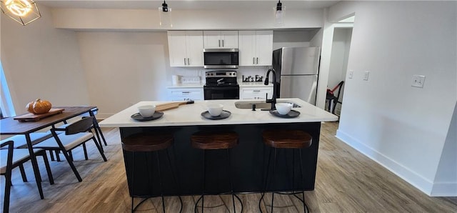 kitchen featuring stainless steel appliances, wood-type flooring, an island with sink, and white cabinets