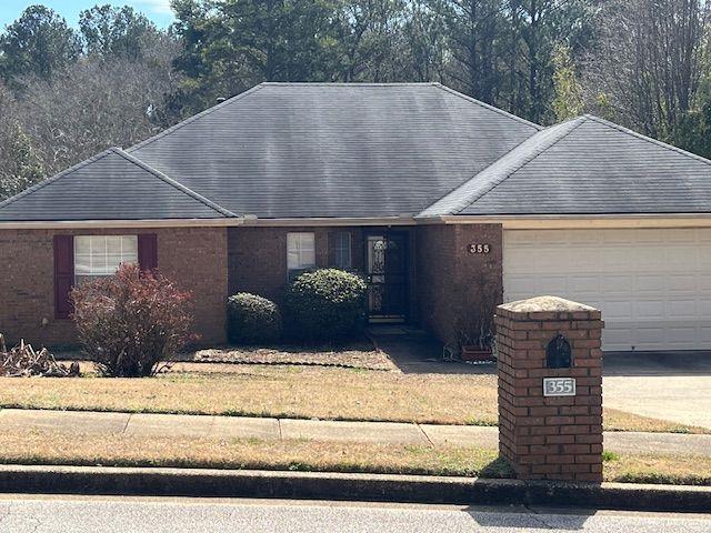 ranch-style house with brick siding, an attached garage, a shingled roof, and a front yard