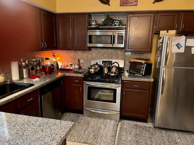 kitchen featuring a toaster, light stone countertops, tasteful backsplash, and appliances with stainless steel finishes