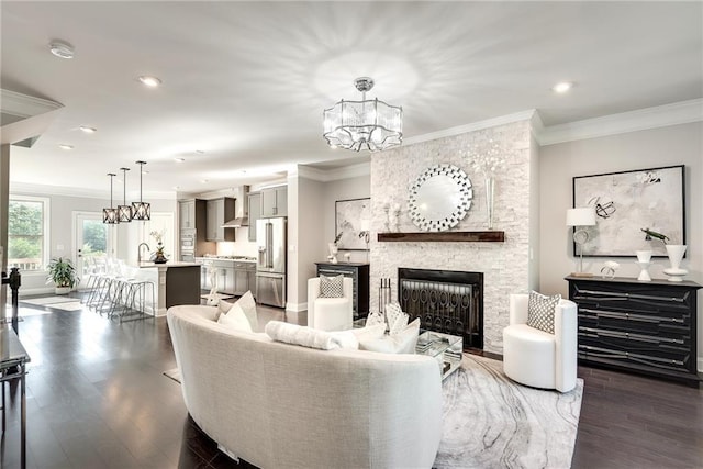 living room with a notable chandelier, dark wood-type flooring, a fireplace, and ornamental molding