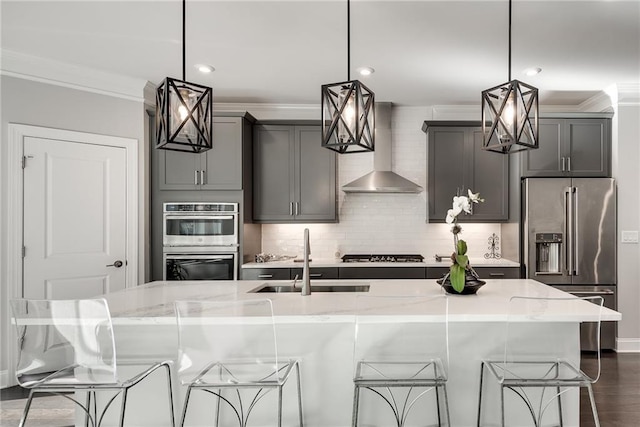 kitchen with stainless steel appliances, sink, pendant lighting, and wall chimney exhaust hood