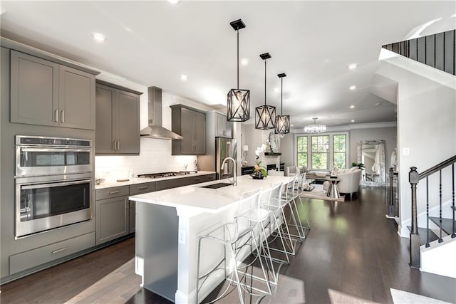 kitchen featuring wall chimney exhaust hood, gray cabinetry, hanging light fixtures, a kitchen breakfast bar, and stainless steel appliances