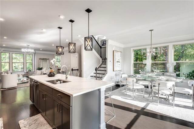 kitchen featuring sink, dark wood-type flooring, light stone counters, an island with sink, and decorative light fixtures