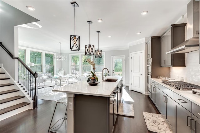 kitchen with sink, a kitchen breakfast bar, pendant lighting, a kitchen island with sink, and wall chimney range hood