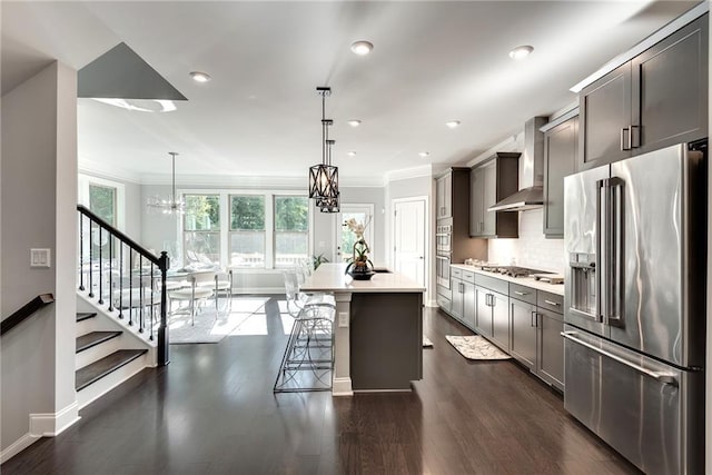 kitchen featuring pendant lighting, appliances with stainless steel finishes, an island with sink, and wall chimney range hood