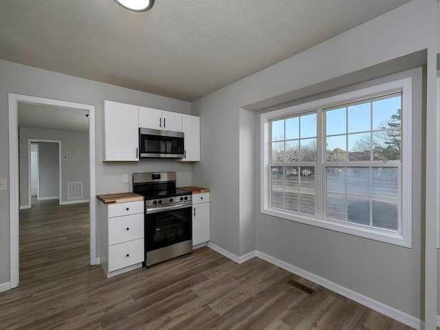 kitchen featuring butcher block countertops, dark wood-type flooring, appliances with stainless steel finishes, a textured ceiling, and white cabinets