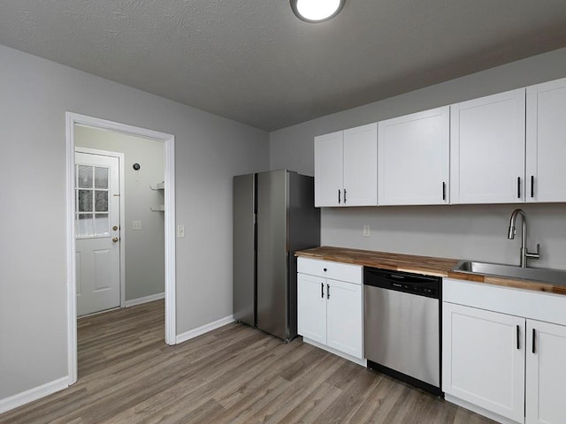 kitchen featuring butcher block countertops, sink, white cabinets, stainless steel dishwasher, and light wood-type flooring