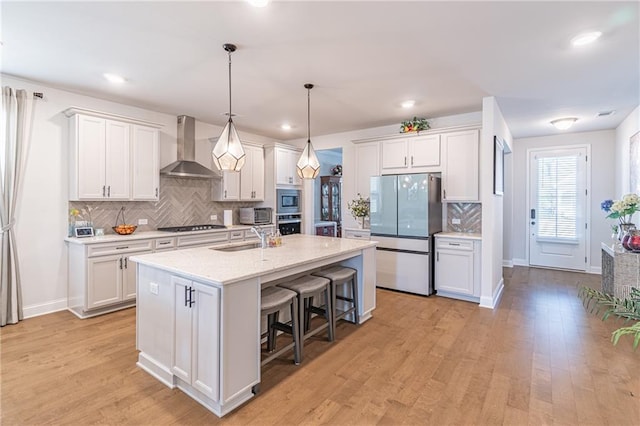 kitchen with wall chimney range hood, white cabinets, and appliances with stainless steel finishes