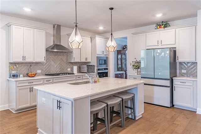 kitchen featuring appliances with stainless steel finishes, wall chimney exhaust hood, light hardwood / wood-style flooring, and white cabinets