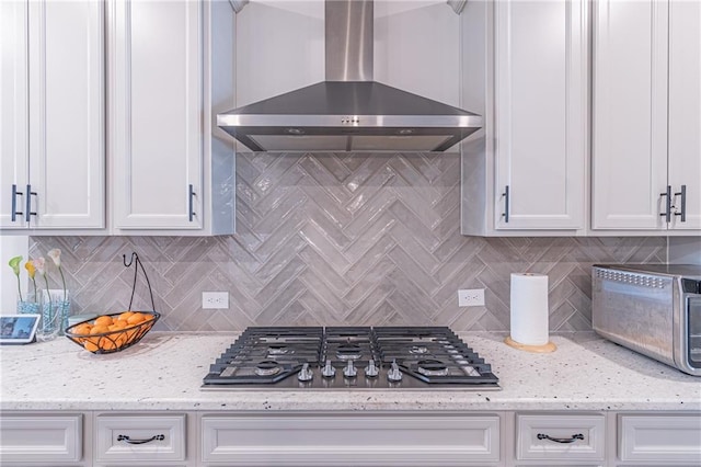 kitchen featuring wall chimney range hood, stainless steel gas stovetop, and white cabinets