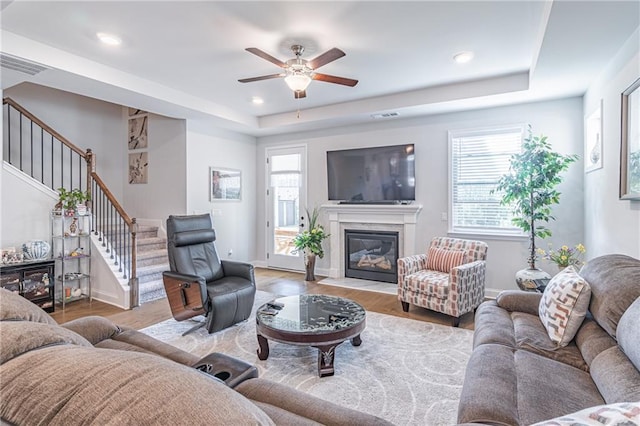 living room featuring a tray ceiling, light wood-type flooring, and ceiling fan