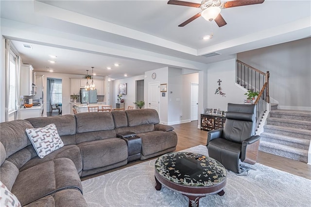 living room featuring ceiling fan with notable chandelier, a tray ceiling, and hardwood / wood-style floors