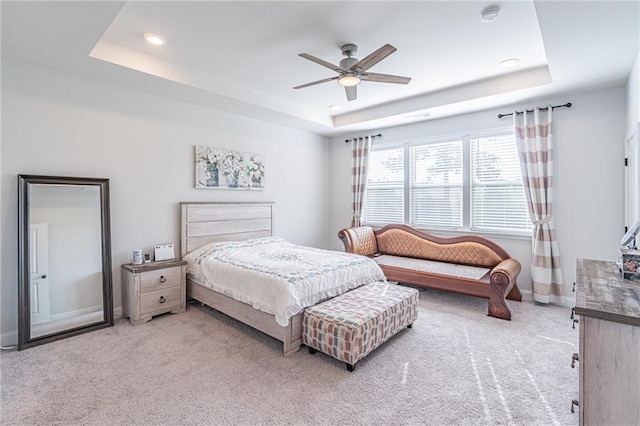 bedroom with light colored carpet, ceiling fan, and a raised ceiling